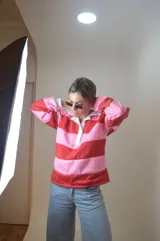 Sweater estilo rugby a rayas horizontales rosas y rojas con cuello blanco y cierre parcial con botones.