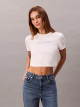Remera cropped blanca de manga corta y cuello redondo, con logo gráfico de Calvin Klein impreso en el pecho.