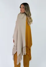 Ruana de punto bicolor, con un lado marrón y otro lado beige con detalle de bordado floral y flecos en los bordes inferiores.