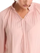 Blusa de gasa con plisado soleil, cuello a la base fruncido con escote en V regulable mediante lazos, y mangas largas abullonadas con puños sastreros.