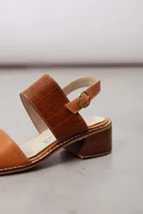 Sandalia de cuero vacuno color tostado con taco bajo y ancho, tira frontal lisa y tira ancha con textura de cocodrilo en el empeine, y tira ajustable al talón con hebilla metálica.