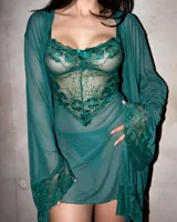 Babydoll de encaje verde oscuro con transparencias, tirantes finos y detalle de moño en el centro del escote. Incluye bata a juego con mangas anchas de encaje y tanga hilo.