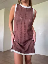Vestido corto de tejido de punto color marrón con detalles calados en franjas verticales y horizontales, cuello redondo y ribetes blancos en contraste.