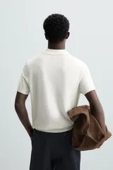 Polo de punto negro, manga corta, con cuello solapa y cierre frontal de tres botones. Presenta un calce regular y acabados en rib en mangas y ruedo.