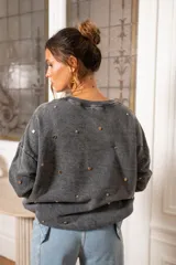 Sweater de corte oversize color beige, confeccionado en algodón. Presenta un diseño holgado con cuello redondo, puños y ruedo acanalados, decorado con múltiples apliques metálicos circulares en tonos dorados y plateados distribuidos por toda la prenda.