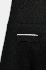 Vestido corto de tejido bouclé en color negro, con escote recto y mangas cortas abullonadas. Presenta detalles de vivos en color blanco a contraste en el escote, el centro del delantero y en los falsos bolsillos frontales.