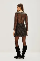 Vestido corto de manga larga con diseño semitransparente y estampado floral geométrico en tonos oscuros y dorados. Presenta un corte entallado en la cintura y una falda con caída fluida.