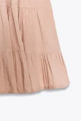 Vestido corto negro de gasa con escote recto y tirantes finos ajustables. El corpiño tiene fruncido elástico y el ruedo es escalonado con volados. Presenta un detalle de encaje a tono en el borde del escote.