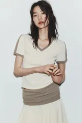 Camiseta slim fit de color blanco crudo con escote en pico y ribetes marrones en el cuello y las mangas.