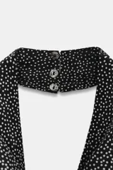 Vestido midi con cuello halter fluido y hombros descubiertos. Presenta un diseño de espalda descubierta, corte evasé y cierre con botones en el cuello. Confeccionado en una mezcla de algodón y viscosa con estampado de lunares pequeños.