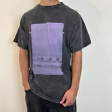Remera de corte oversize con efecto de lavado ácido en color negro. Presenta un estampado rectangular central en tonos violeta con la palabra 'VISIONS' y una escena de surfistas en el mar.