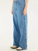 Pantalón de jean celeste, de corte wide leg y tiro medio, con cordones entrelazados a lo largo de los laterales.