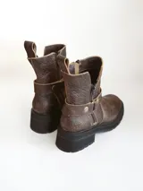 Bota corta de cuero vacuno en color chocolate con efecto desgastado. Presenta una suela track de goma negra, detalle de pulsera desmontable con tachas metálicas y cierre lateral.