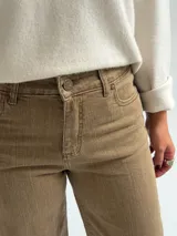 Jean de corte recto y tiro medio, en color camel con acabado desgastado. Presenta diseño clásico de cinco bolsillos, cierre frontal con botón y cremallera, y costuras reforzadas en el ruedo.