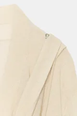 Chaqueta de punto fino color beige, con escote fluido y drapeado, manga larga y cierre frontal cruzado.