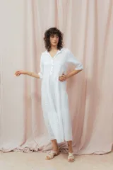 Vestido midi blanco de lino, con cuello camisero, botonera frontal y mangas 3/4. Presenta un calce relajado con frunces en la cintura.