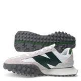Championes urbanos New Balance modelo XC-72, con diseño combinado en blanco, gris y verde. Presentan una silueta retro-futurista con superposiciones de gamuza, paneles de cuero y una suela de goma dentada distintiva que se extiende hacia la puntera.
