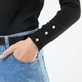 Sweater de punto ligero color negro, con cuello redondo, manga larga y detalle de botones metálicos en los puños.