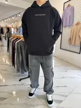 Canguro oversize negro con capucha y bolsillo tipo canguro. Presenta el texto "TOP STYLE COLLECTIONS" en el pecho y un estampado gráfico en la espalda con óvalos y texto en tonos celestes y blancos.