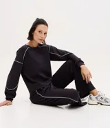 Buzo deportivo de corte oversized color negro, con cuello redondo, mangas largas y detalles de frisos contrastantes en color blanco. Confeccionado en una mezcla de modal, poliéster y elastano.