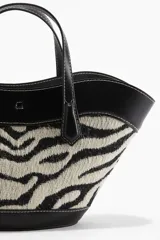 Cartera tipo tote con diseño de estampado animal print de cebra, confeccionada en tejido jacquard con detalles en material sintético negro. Cuenta con doble asa de mano, correa larga ajustable y extraíble para usar como bandolera, y cierre interno de mosquetón.