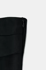 Vestido midi de escote strapless y hombros descubiertos, confeccionado en tejido negro combinado con detalle drapeado en la parte frontal de la falda. Presenta un diseño entallado y cierre lateral con cremallera oculta.