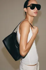 Bolso de hombro de piel color negro, con diseño estructurado, solapa superior y correa ajustable para el hombro.