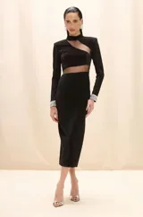 Vestido midi negro de corte ajustado, con mangas largas, cuello alto y aberturas estratégicas con paneles de tul transparente en el pecho y la cintura. Presenta puños decorados con aplicaciones de cristales brillantes.
