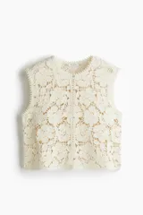 Chaleco sin mangas de punto crochet color crema, con diseño floral calado y ribetes de picot en cuello, sisas y ruedo. Cierre frontal con botones nacarados.
