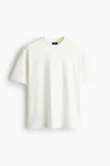 Remera de algodón pesado color blanco, con cuello redondo ribeteado, hombros caídos y mangas cortas de corte holgado.