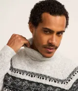 Suéter de punto gris con cuello alto y manga larga. Presenta textura jacquard y estampa horizontal étnica en tonos negros y grises.