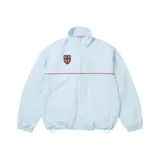 Campera Supreme de nylon color celeste, con cuello alto, cierre frontal y una línea horizontal roja en el pecho. Cuenta con escudo bordado y puños y ruedo elásticos.