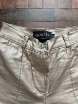 Pantalón de tiro alto confeccionado en eco cuero con acabado metalizado dorado. Presenta un corte recto con aberturas laterales con cierre en los tobillos y costuras frontales decorativas.