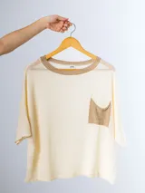 Remera tejida color crema con cuello redondo y bolsillo frontal verde.