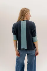 Buzo de punto en color negro con mangas tres cuartos y puños en contraste color marrón. Presenta un diseño holgado con tajos laterales y un aplique circular con logo en la parte inferior.