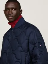 Campera bomber azul marino con diseño acolchado, cuello estilo béisbol, cierre de cremallera, dos bolsillos delanteros ribeteados, cuello, puños y bajo de punto canalé y parche con el logo de Tommy Hilfiger en la manga.