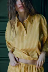 Camisa de corte holgado confeccionada en mezcla de lyocell, con estampado de rayas verticales en tonos amarillos y blancos. Presenta cuello solapa, cierre frontal parcial con botones y mangas anchas por debajo del codo.