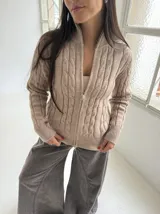 Sweater tipo campera de punto con cierre frontal completo y cuello alto. Presenta un diseño de tejido trenzado vertical y mangas largas, ofreciendo un estilo clásico y versátil.