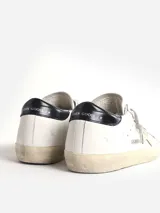 Zapatillas urbanas Golden Goose modelo Super-Star, de cuero blanco con estrella plateada en el lateral, detalle de talón en cuero negro y suela de goma color crema con efecto desgastado.