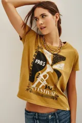 Remera de algodón color mostaza con estampa frontal estilo vintage que incluye un diseño de trompeta, piano y la inscripción '1983 Live Jazz Festival'. Presenta cuello redondo y mangas cortas.