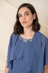 Vestido corto de gasa en color azul, compuesto por un vestido sin mangas con escote redondo decorado con pedrería y una capa corta superpuesta con mangas anchas y diseño en capas escalonadas.