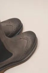 Bota tipo Chelsea de cuero vacuno color suela, con diseño brogue en la puntera y laterales. Presenta paneles elásticos laterales en color marrón oscuro, tirador trasero y suela de goma con plataforma.