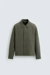 Sobrecamisa de corte boxy fit confeccionada en tejido compacto color verde militar. Presenta cuello solapa, cierre frontal con botones, mangas largas con puños abotonados y bolsillos laterales integrados en la costura.