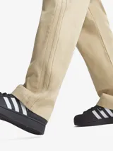 Pantalón de corte holgado color beige, con bolsillos delanteros y traseros. Presenta cintura elástica con cordón de ajuste y tres líneas verticales a los costados.