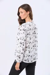 Blusa blanca de manga larga con estampado de hojas pequeñas en gris. Tiene cuello redondo, cierre frontal con botones personalizados y mangas abullonadas con puños elásticos.