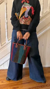 Matera de cuero con diseño de paneles verticales en combinación de colores azul, verde, marrón y bordó. Cuenta con dos asas cortas de cuero y estructura rígida.