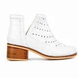 Botín de cuero blanco con textura de crocco y charol, diseño con calados circulares y aberturas laterales en forma de V. Cuenta con taco foliado de madera y vira cosida.