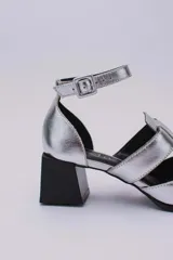 Sandalias plateadas con punta cerrada, tiras entrecruzadas y pulsera al tobillo con hebilla. Taco cuadrado negro.