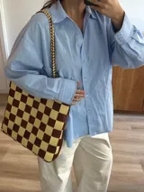 Bolso tipo tote de cuero trenzado a mano con diseño de damero en colores marrón y beige. Cuenta con doble asa trenzada y forro interior.