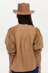 Blusa color tostado confeccionada en lino, con mangas abullonadas de ramie y detalles de bordado en punto smock en los puños.